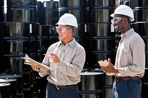 two engineers smiling with barrels in background